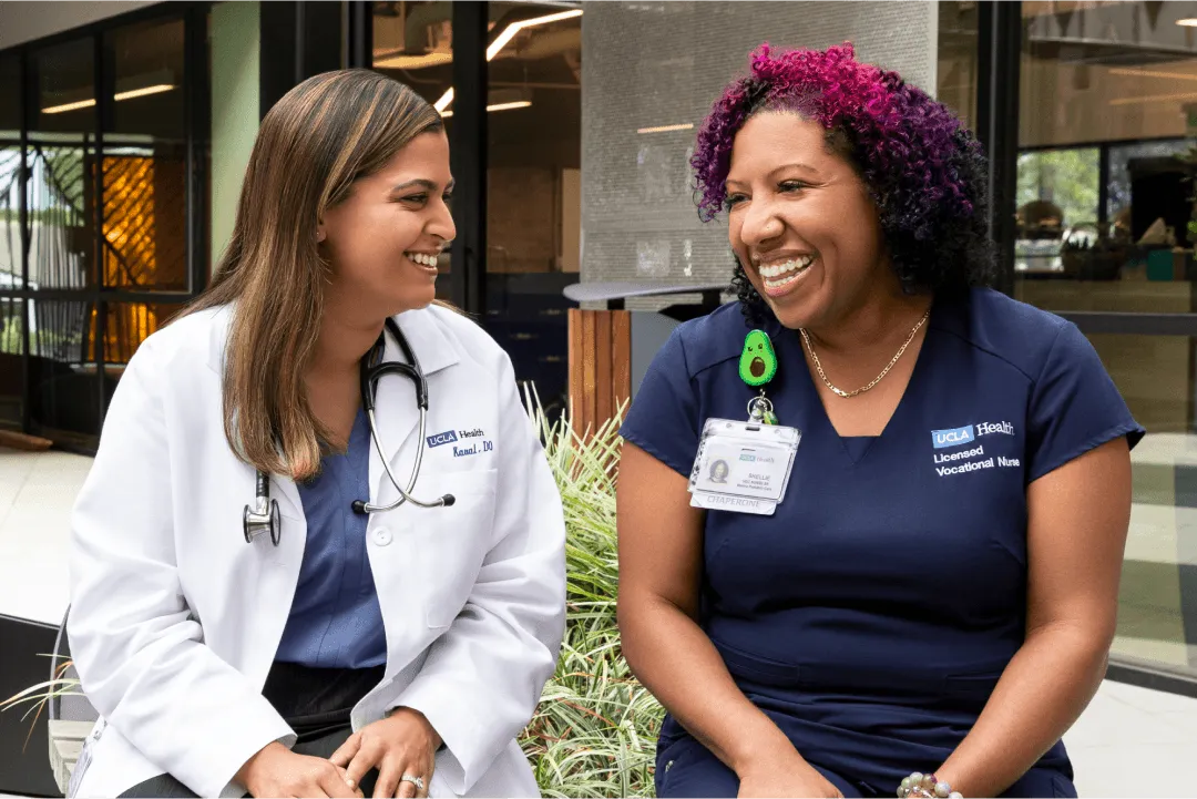 A female UCLA Health physician and a female UCLA Health nurse enjoying a casual conversation in a hospital courtyard